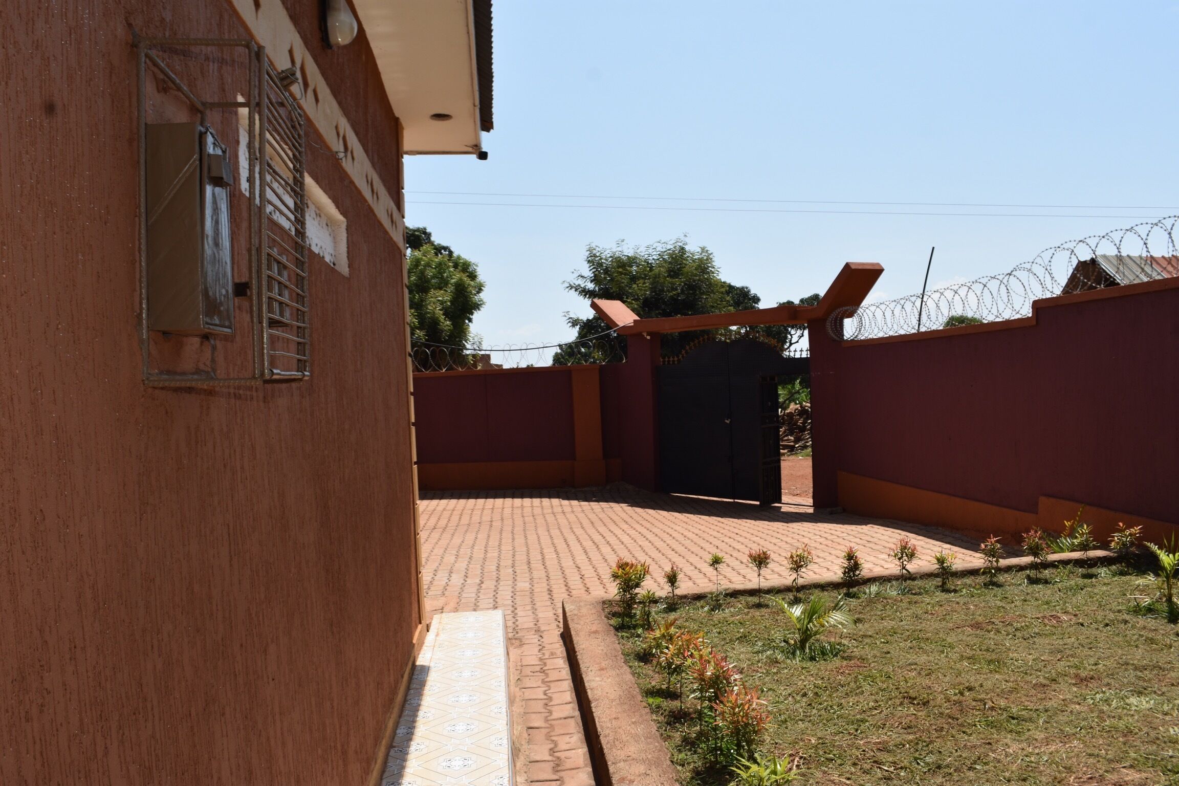 A building with a brick exterior, a gated entrance, and a small garden area with young plants.