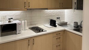 A modern kitchen with wooden cabinets, a microwave, a kettle, and a sink. - Urban Muse V - Archaeological Museum of Athens (Athina)