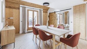 Un espace repas moderne avec une table en bois et des chaises rouges, de grandes fenêtres et une vue sur l’extérieur.