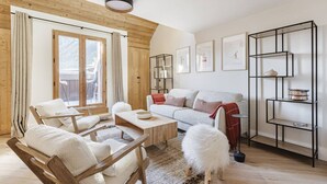 Un salon chaleureux avec un plafond en bois, un canapé blanc, une table basse en bois et un petit tabouret moelleux blanc.