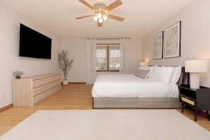 A bedroom with a bed, bedside tables, a ceiling fan, a TV, and a window with curtains.