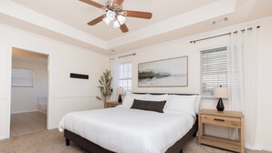 A bedroom with a large bed, a ceiling fan, a nightstand with a lamp, a painting on the wall, and a window with blinds. - Pet Friendly 3BR | Fenced Yard + Near RAFB (Warner Robins)