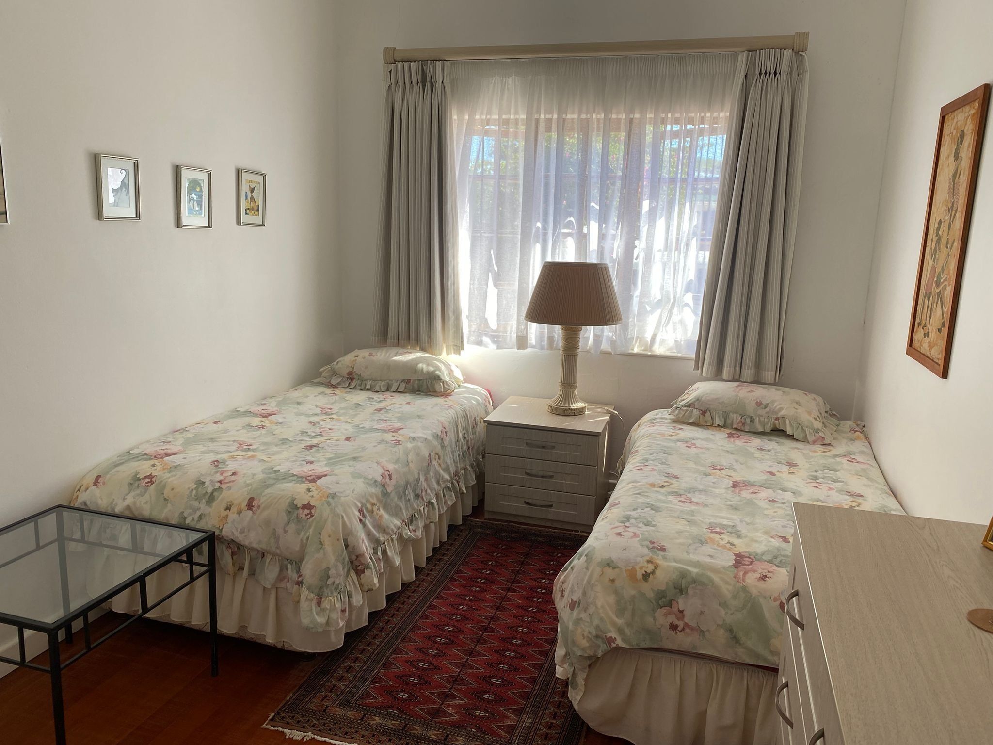 Une chambre avec deux lits simples, une petite table, une lampe, une table en verre et un tapis rouge à motifs.
