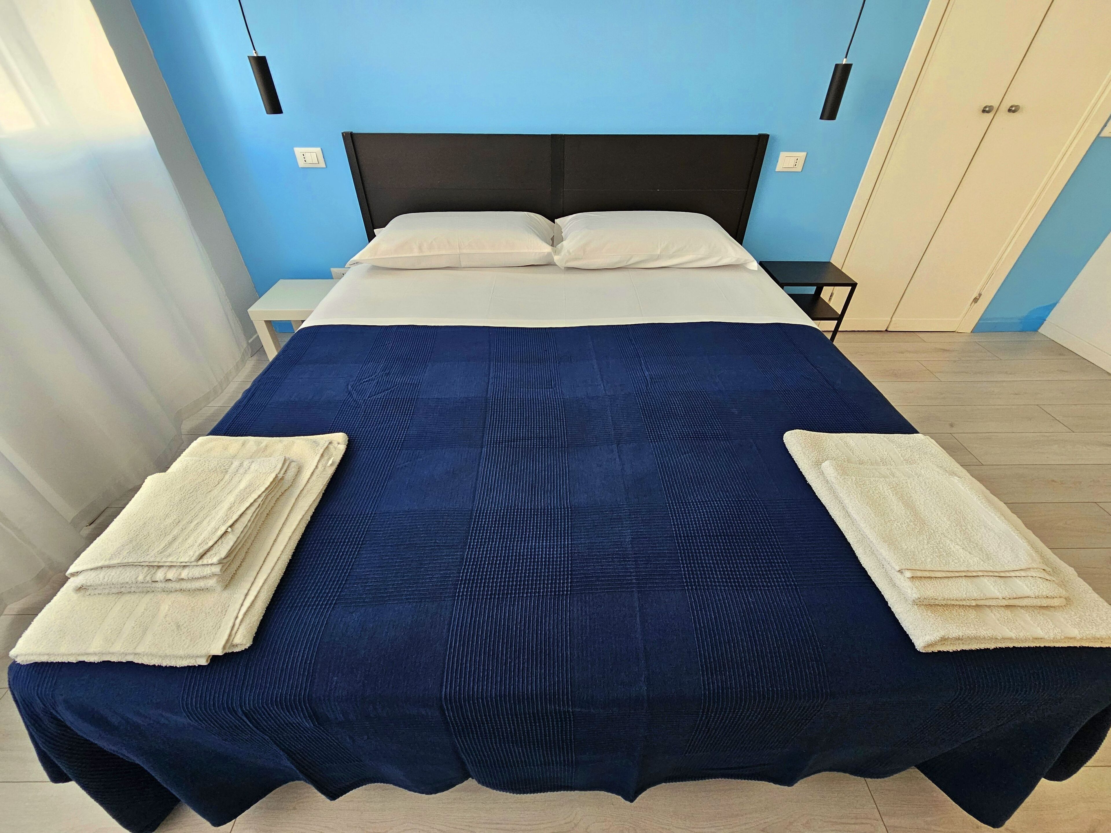 A neatly made bed with a dark blue bedspread and two folded towels on each side.