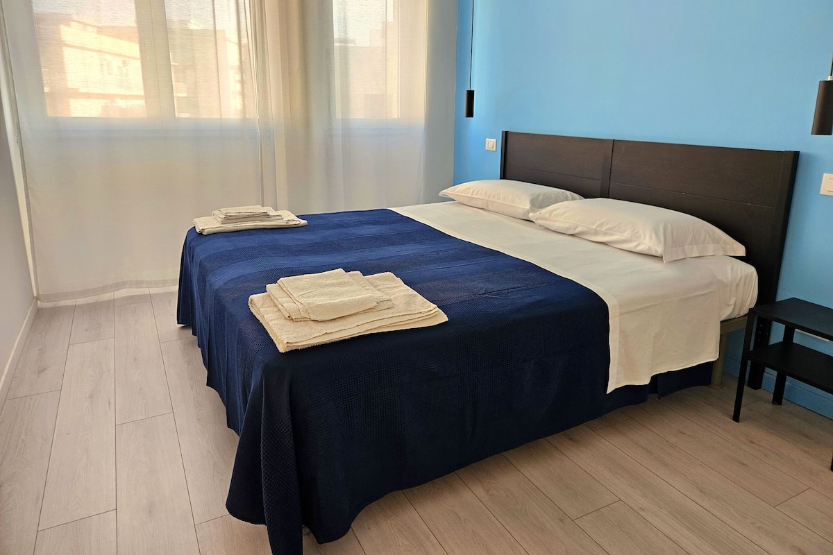 Une chambre d’hôtel avec un lit, une table de chevet et une fenêtre ornée de rideaux légers.