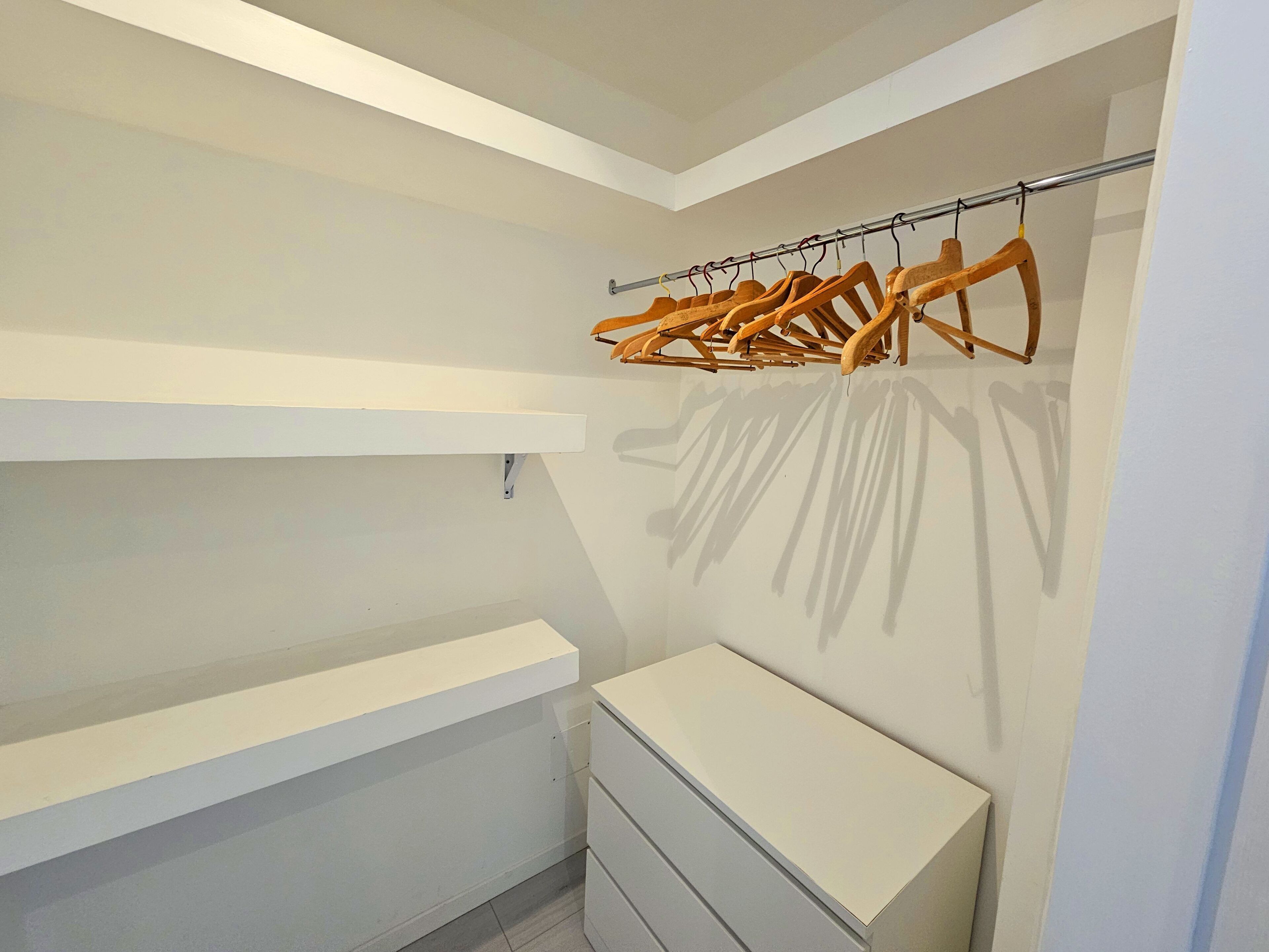 Un dressing ouvert avec des étagères blanches, un porte-manteau en bois et une commode blanche.