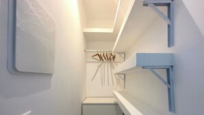 Un couloir étroit avec une porte blanche, un interrupteur et un porte-manteau sur lequel sont suspendus des vêtements.