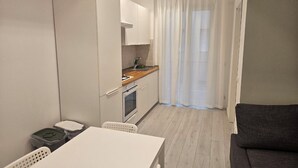 Une cuisine compacte comprenant une table et des chaises, un petit four et un évier. Un canapé se trouve dans l’espace salon.