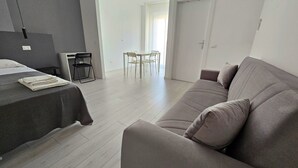 Une pièce moderne et bien éclairée, comprenant un lit, un canapé gris et un coin repas avec des chaises et une table.