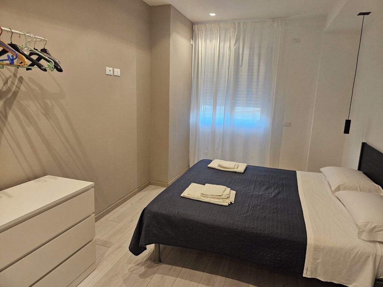 Ein Schlafzimmer mit Bett, Nachttisch, Kleiderschrank und einem Fenster mit Vorhängen.