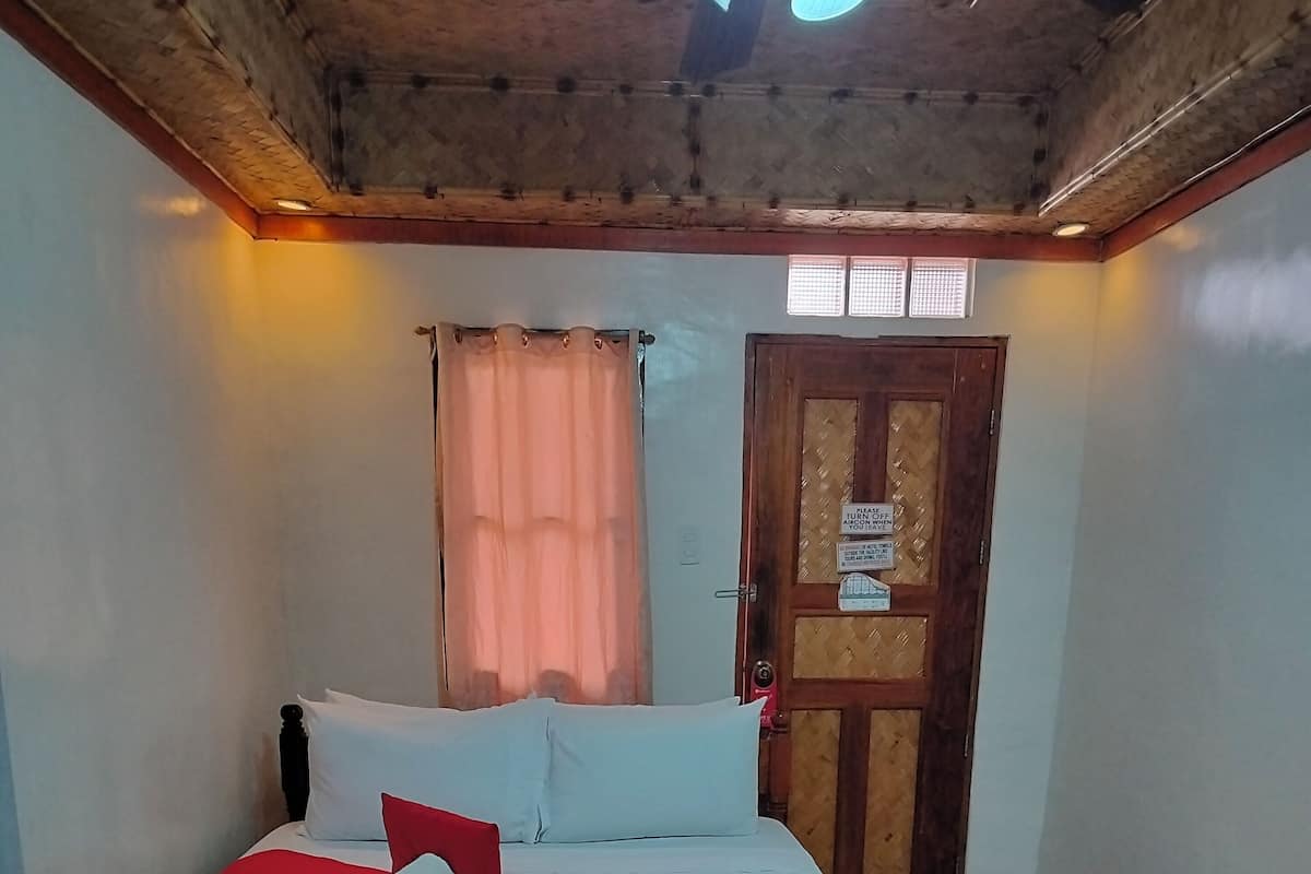 Uma cama bem arrumada com lençóis brancos e um corredor vermelho, uma porta de madeira com uma placa e um chão estampado.