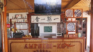 Un comptoir d’accueil en bois portant l’inscription « AMPHIBI-KO RESORT » et surmonté d’un écran de télévision.