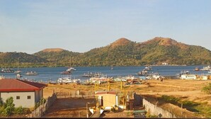 Un port de plaisance sur la côte, avec des bateaux amarrés, un petit bâtiment doté d’un toit rouge et, au loin, un paysage vallonné.