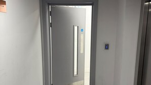 Ein Flur mit einer Tür zu einem Zimmer, einem an der Wand montierten Lichtschalter und einem Boden mit grauem Fliesendesign.