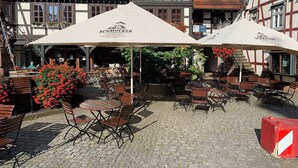 An outdoor seating area with tables and chairs, umbrellas, and a cobblestone floor. - Living by the historic town hall (Michelstadt)