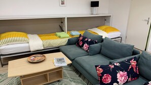 A compact room with a sofa, a bed with yellow and white bedding, a small table with a tray, and a wall-mounted TV. - Living by the historic town hall (Michelstadt)