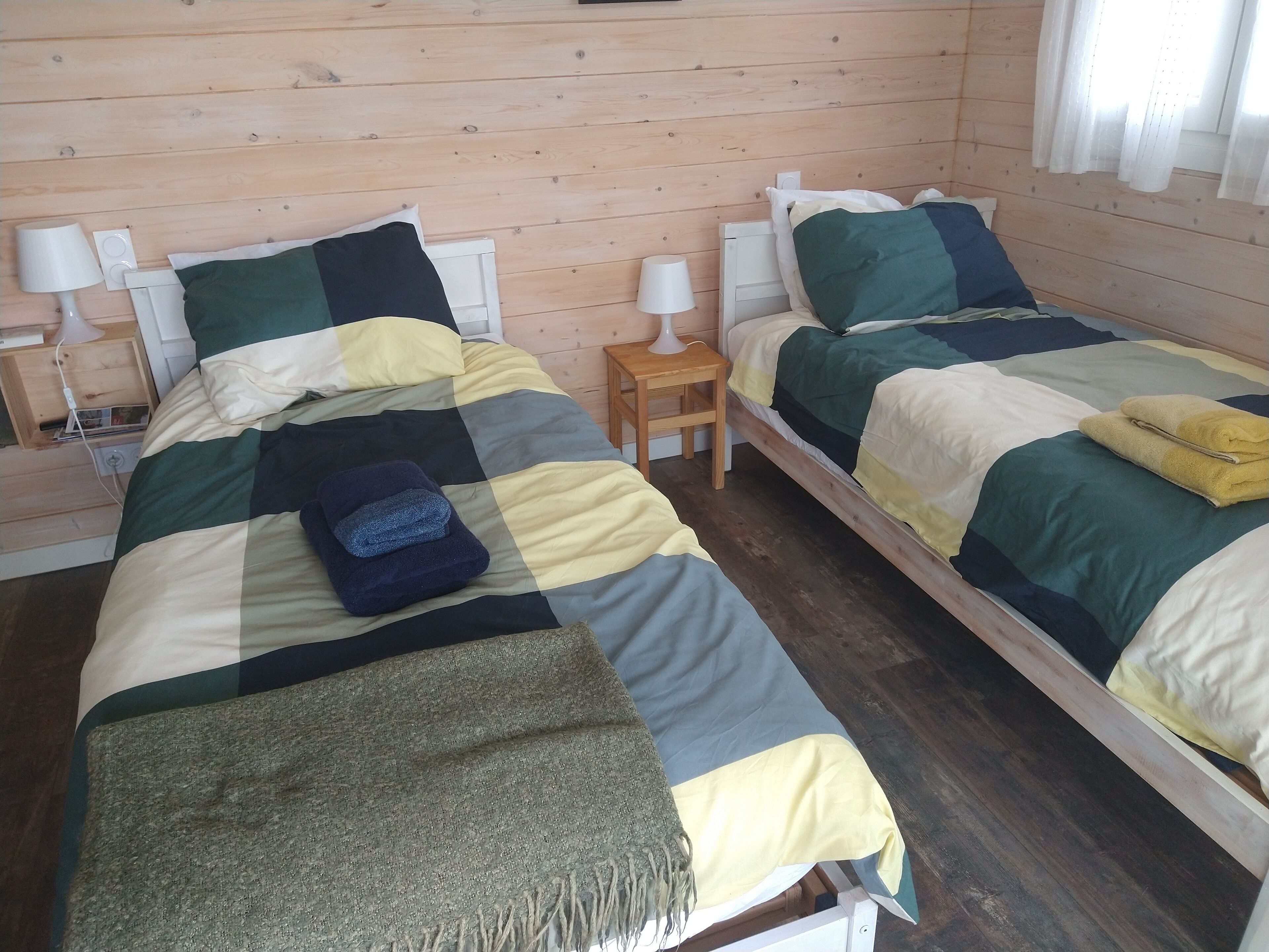 A room with two single beds, each with a wooden headboard, a small bedside table with a lamp, and a wooden nightstand with a lamp.