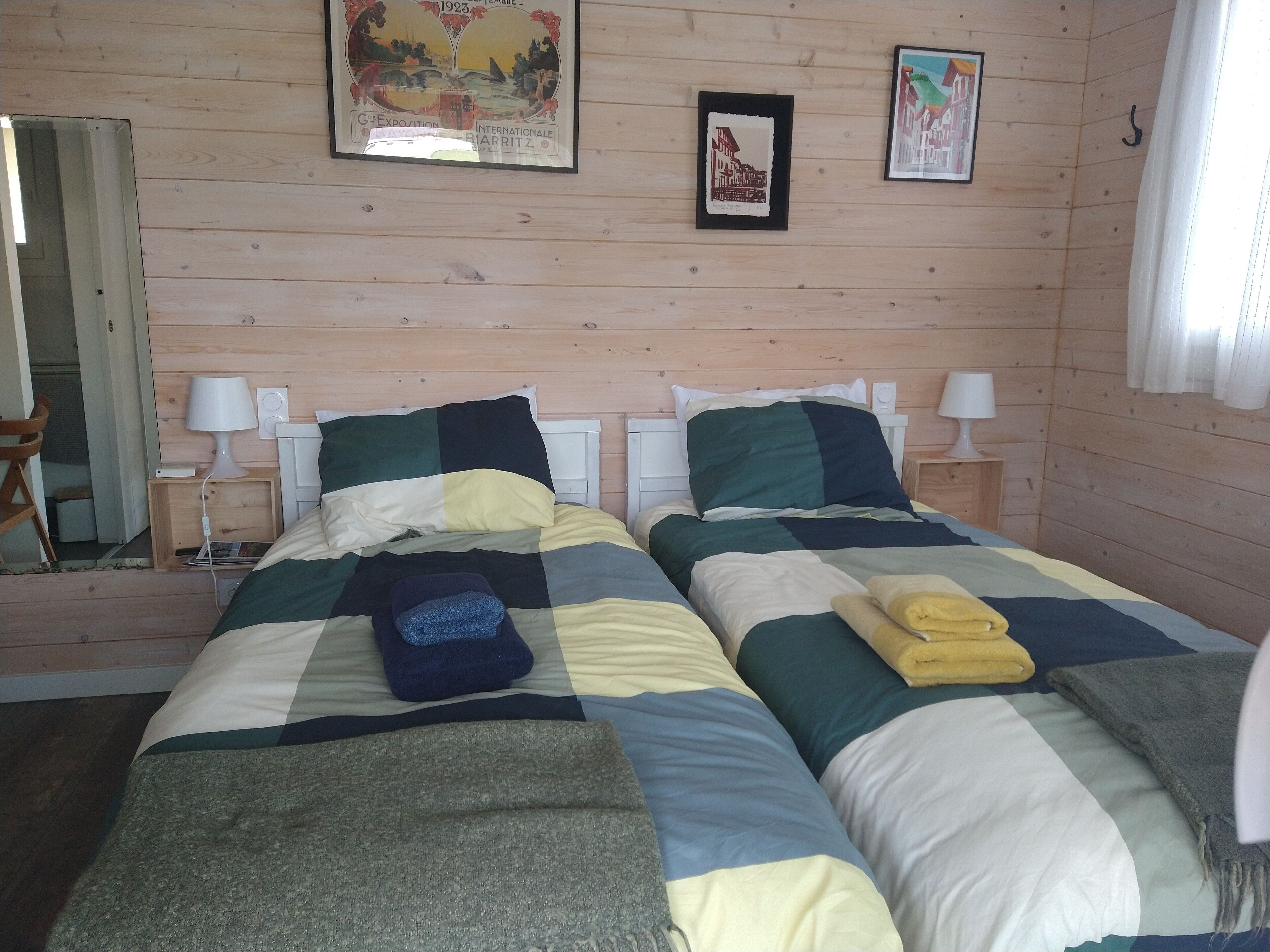 A room with two beds, wooden walls, and framed pictures on the wall.