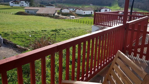Un balcón con barandilla roja que da a un campo verde y casas a lo lejos.