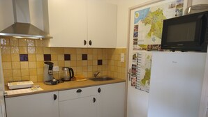 Cocina compacta con armarios blancos, microondas, cafetera y lavamanos.