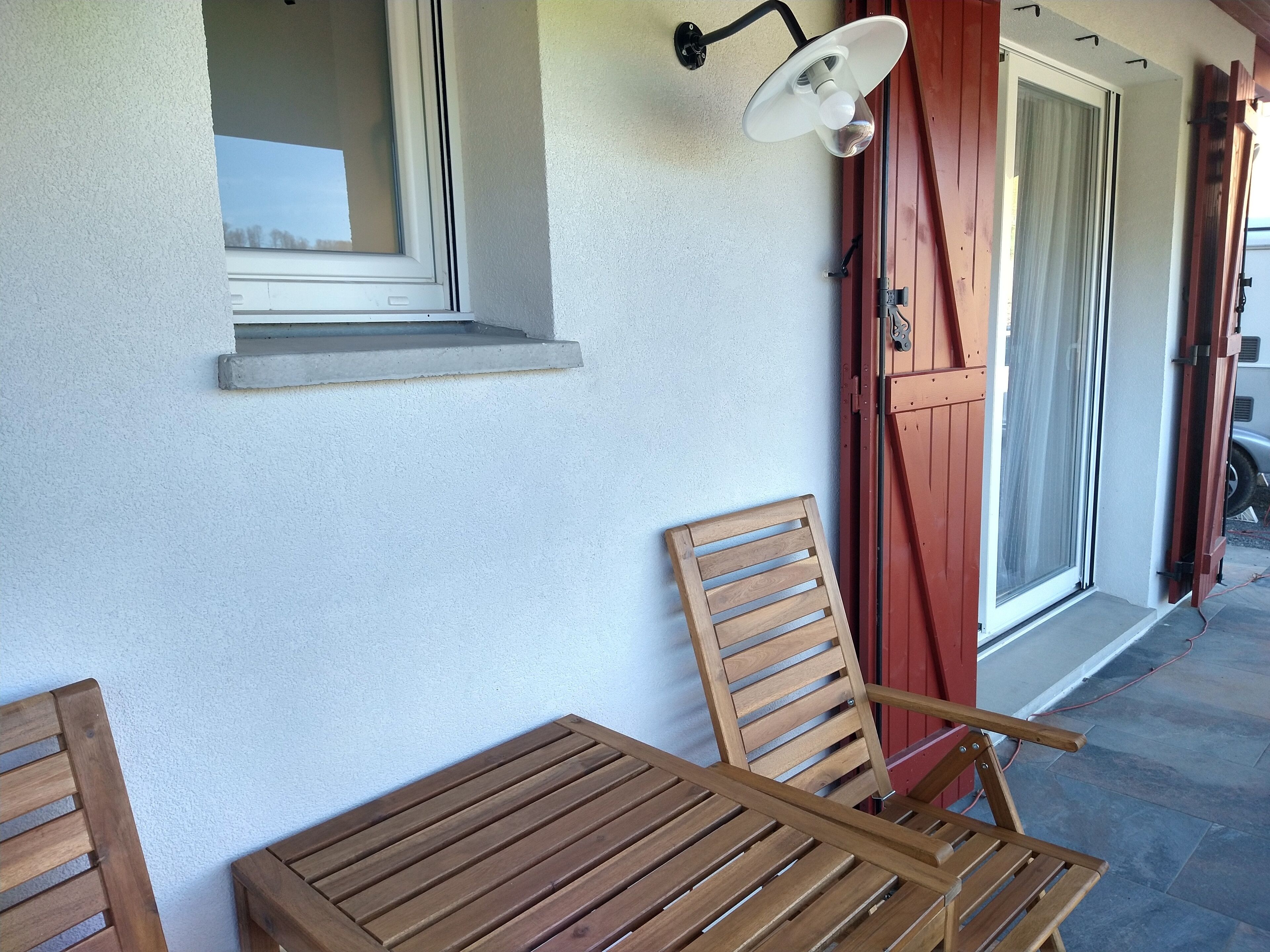 A wooden table and chairs outside a building with a window and a door.
