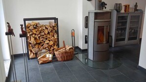 A room with a fireplace, a wall-mounted shelf with books, and a tiled floor. - Quiet vacation home with lots of space (Masserberg)