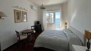 A hotel room with a bed, a desk, a chair, a TV, and a balcony with a view of the sea. - Sea view apartment in the city center, 3 minutes from the station and port (Salerno)