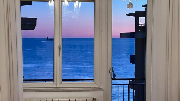 A view from a window overlooking a body of water at sunset, with a balcony and railing visible. - Sea view apartment in the city center, 3 minutes from the station and port (Salerno)