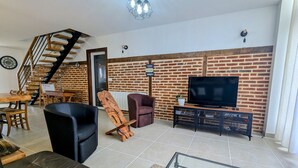 Een woonkamer met een bakstenen muur, een televisie, een bank, een stoel, een salontafel en een trap.