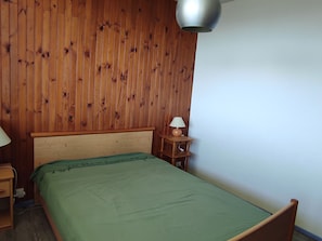A bedroom with a wooden headboard, a green bedspread, a bedside table with a lamp, and a wall-mounted light fixture. - 2-room apartment with view, near slopes and lake (Besse-et-Saint-Anastaise-Super Besse)