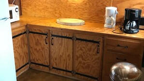 Una cocina compacta con armarios de madera, microondas, cafetera y pileta de acero inoxidable.