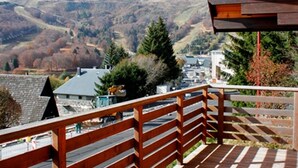 A wooden balcony with a view of a town and hills in the background. - Unique chalet near slopes, sleeps 9, original artworks (Besse-et-Saint-Anastaise-Super Besse)