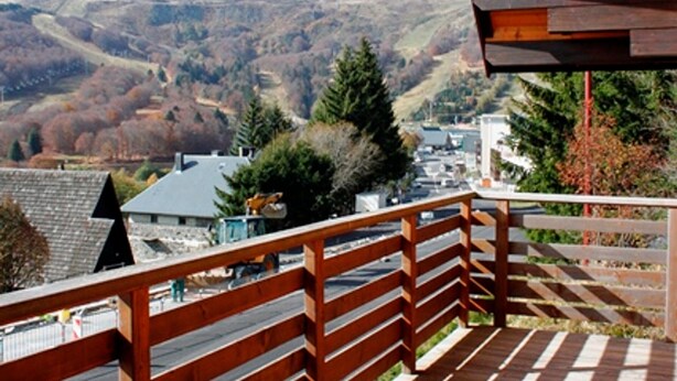 Un balcón de madera con vista a un pueblo y colinas al fondo.