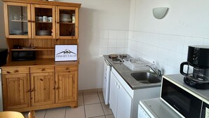 Una cocina compacta con armarios de madera, un microondas, una cafetera y un refrigerador pequeño.