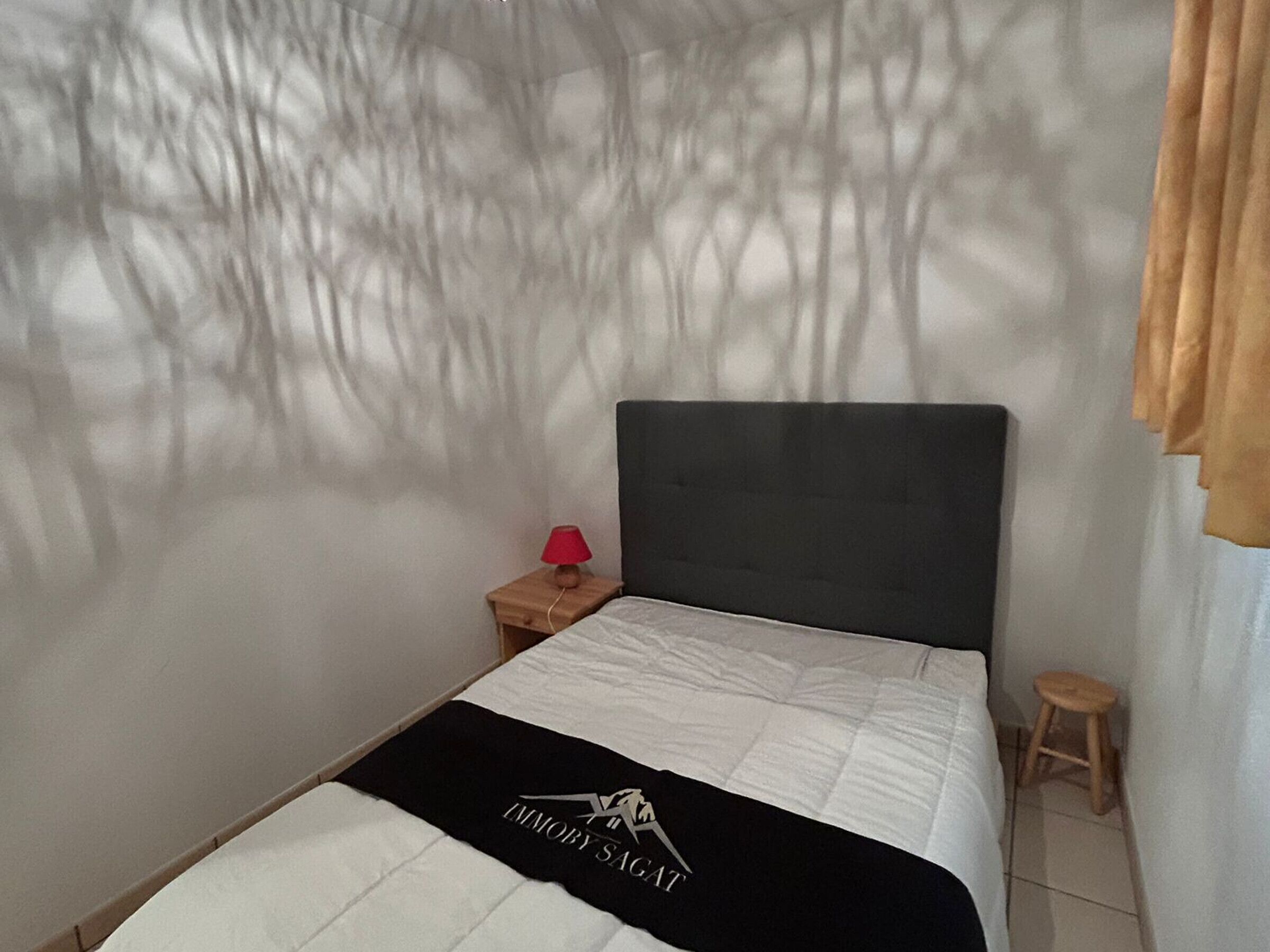 Un dormitorio con una cama, una mesita de noche, una lámpara roja y un taburete pequeño.