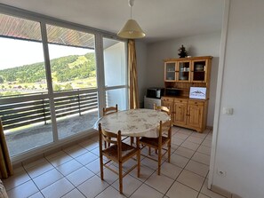 A dining area with a table and chairs, a kitchen with cabinets, and a large sliding glass door with a view of a green landscape. - Apt for 6 with Private Parking, near Lake and ski (Besse-et-Saint-Anastaise-Super Besse)