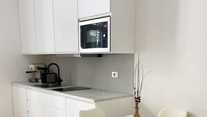 A compact kitchen with white cabinets, a built-in microwave, a coffee maker, and a small dining table with chairs.