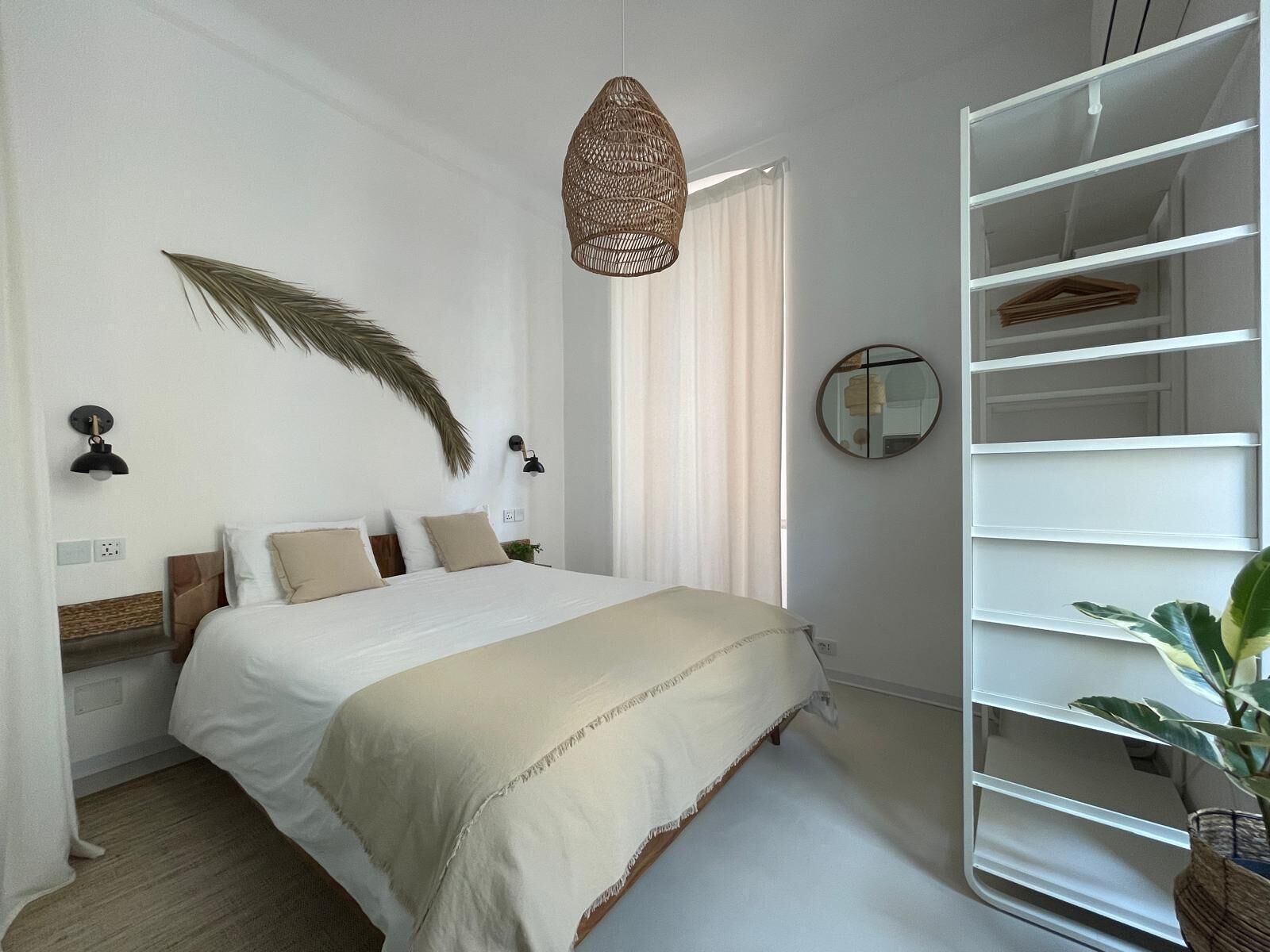 A bedroom with a bed, a hanging light fixture, a mirror, and a white shelving unit.