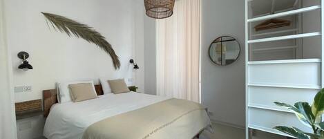 A bedroom with a bed, a hanging light fixture, a mirror, and a white shelving unit.
