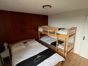 Ein Schlafraum mit Etagenbetten, einem Holzkopfende, einem Nachttisch mit Lampe und einer Tür rechts.