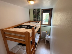 Ein kleines Zimmer mit einem Einzelbett und einem Holzbettkasten, einem Fenster mit Blick auf Grünflächen und einem kleinen Nachttisch mit Lampe.