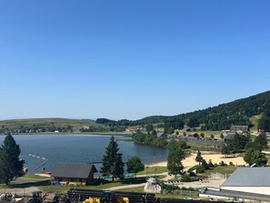 A lakeside view with a clear sky, a sandy beach, and a small building near the water.