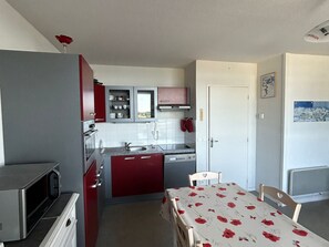 A compact kitchen with red cabinets, a microwave, and a dining area with a table and chairs.