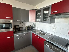 Eine moderne Küche mit roten und grauen Schränken, Edelstahlgeräten und einer gefliesten Rückwand.