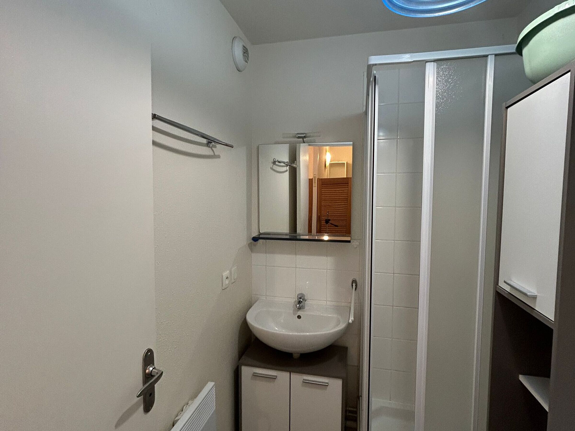 A bathroom with a white sink, a mirror, a towel rack, and a shower enclosure.
