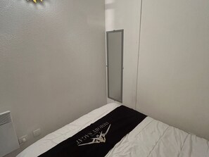 Ein kleines Zimmer mit einem Einzelbett, einer schlichten weißen Wand und einer Tür.