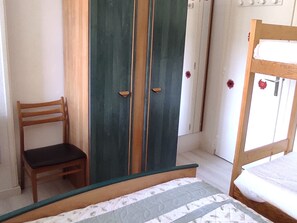 Quarto com cama, uma cadeira de madeira e um guarda-roupa de duas portas.
