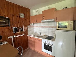 A compact kitchen with wooden paneling, a sink, a stove, a microwave, and a clock. - Cozy 1-bedroom apartment in Super Besse center (Besse-et-Saint-Anastaise-Super Besse)