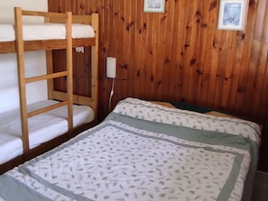 A bunk bed with white bedding, a single bed with patterned bedding, wooden walls, and a framed picture. - Cozy 1-bedroom apartment in Super Besse center (Besse-et-Saint-Anastaise-Super Besse)