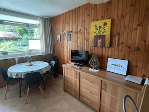 Una habitación con paneles de madera, una mesa de comedor, sillas, un televisor, una piedra decorativa y un cuadro enmarcado.